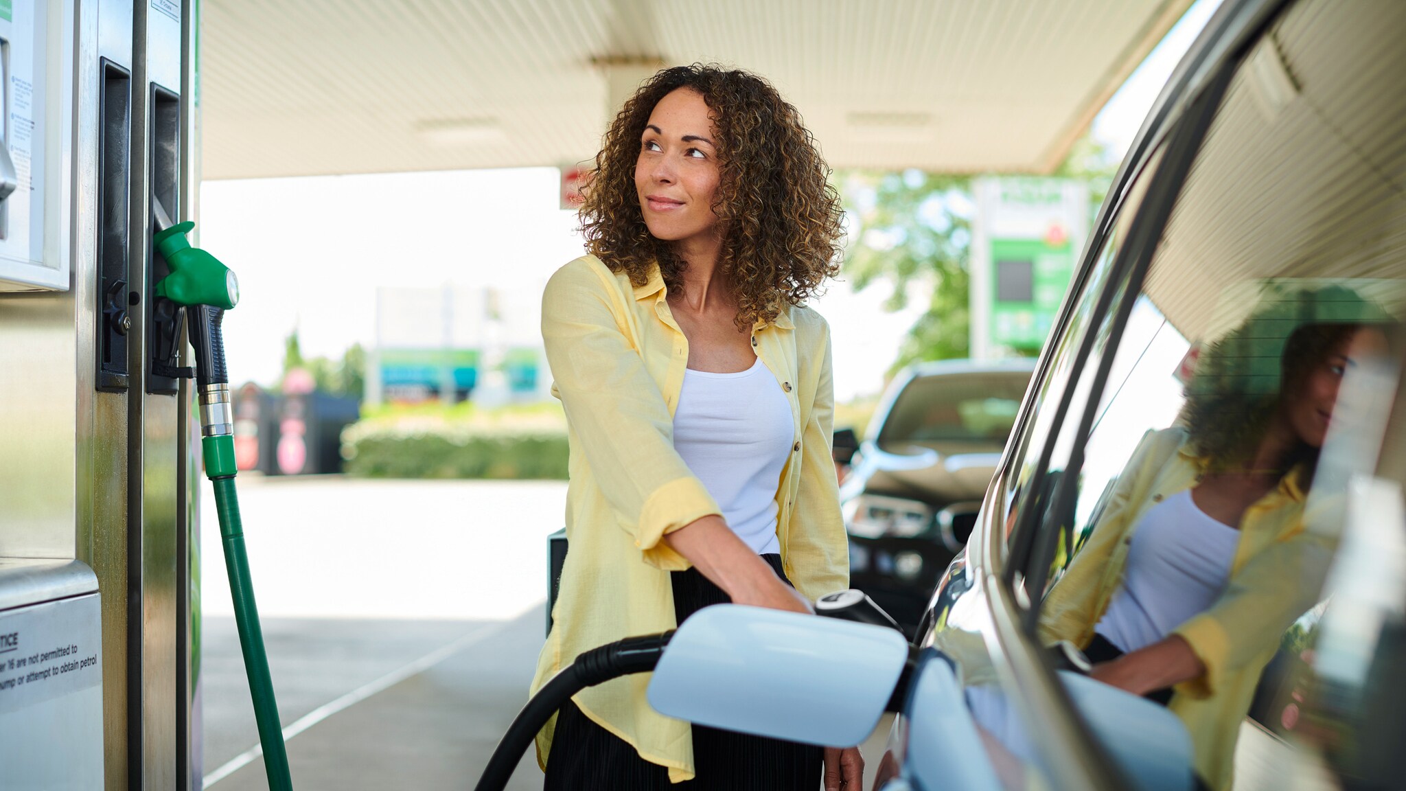 Eine Frau betankt ihr Auto an der Zapfsäule einer Tankstelle.